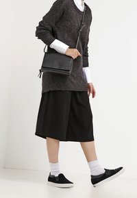 Musta ylikokoinen villapaita, polvipituinen musta hame, mustat liukukengät, valkoiset nilkkasukat ja pieni musta olkalaukku.