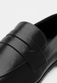 Sort læderloafer med en glat finish, der har et dekorativt topbånd og horisontale rilleaccents. Klassisk design med syningsdetaljer.