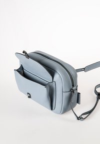 Lichtblauwe leren crossbody tas met een gestructureerd oppervlak, een met rits afsluitbaar hoofdcompartiment en een buitenzak. Inclusief verstelbare schouderband.