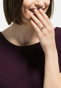 Diamantforlovelsesring med en rund midtsten, sølvring med fine detaljer, båret på en hånd, der rører ved hagen.