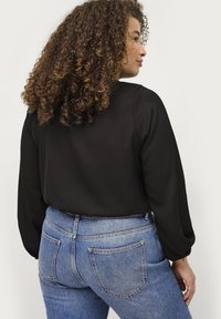 Schwarze Bluse mit langen Ärmeln und glatter Textur, kombiniert mit hochgeschnittenen, hellblauen Jeans mit klassischer Naht und zwei Gesäßtaschen.