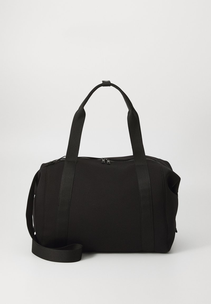 Bolsa de deporte negra con asas gruesas y una correa desmontable. Fabricada en un tejido suave, cuenta con un cierre de cremallera y un diseño minimalista.