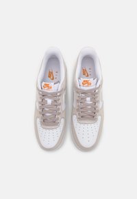 Sneakers Nike Air Force 1 bianchi e beige con tomaia in pelle liscia, accenti grigio chiaro, punta perforata e lacci piatti.