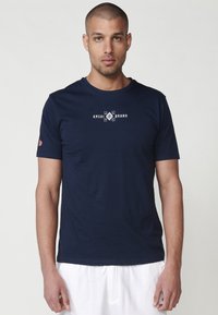 Tamsiai mėlynas trumpomis rankovėmis medvilninis marškinėliai su balta tekstine logotipu "KRSHI BRAND" ant krūtinės, lygaus paviršiaus ir apvaliu iškirpimu.