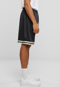 Sorte atletiske shorts med en teksturert stoff, med en stripete kant i gull og hvitt. Stylet med hvite sneakers og ankelsokker.