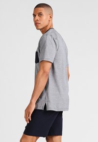 Grijze t-shirt met korte mouwen en een marineblauwe zak, gemaakt van zachte stof, voorzien van zijsplitten, gecombineerd met donkere shorts.