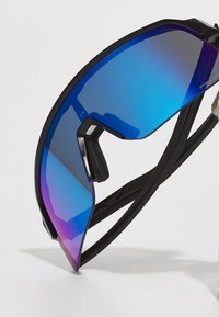 Gafas de sol deportivas con una lente grande y curva en degradado de azul a morado y montura negra. Presentan un diseño elegante y almohadillas nasales ajustables.