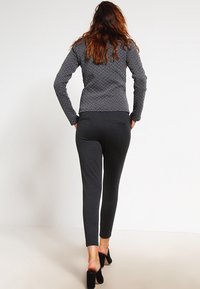 Grå pudejakke med en tekstureret overflade, parret med mørkegrå leggings. Begge dele er tætsiddende og lette. Sorte hæle fuldender looket.