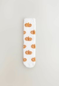 Weißer flauschiger Socken mit einem orangefarbenen Kürbismuster, das über den Stoff wiederholt ist, flach auf einem hellen Hintergrund angezeigt.