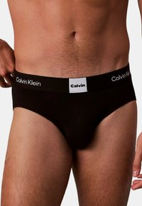 Schwarze Baumwoll-Slips mit einem elastischen Bund mit Markenlogo und weißem Logo-Patch. Glatte Textur und eng anliegendes Design für optimalen Tragekomfort.