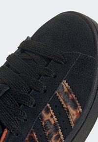 Černé semišové tenisky s černými šňůrkami, které mají texturované akcenty s leopardím vzorem a robustní gumovou podrážku.