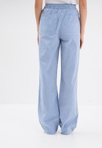 Pantaloni a gamba larga a righe blu e bianche con vita elasticizzata, dotati di due tasche posteriori e di una vestibilità rilassata. Realizzati in tessuto leggero.