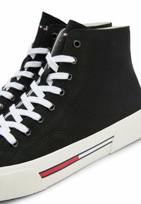 Czarne wysokie trampki z płótna, z białymi sznurówkami, metalowymi oczkami i białą gumową podeszwą, ozdobione czerwonymi i niebieskimi paskami po boku.