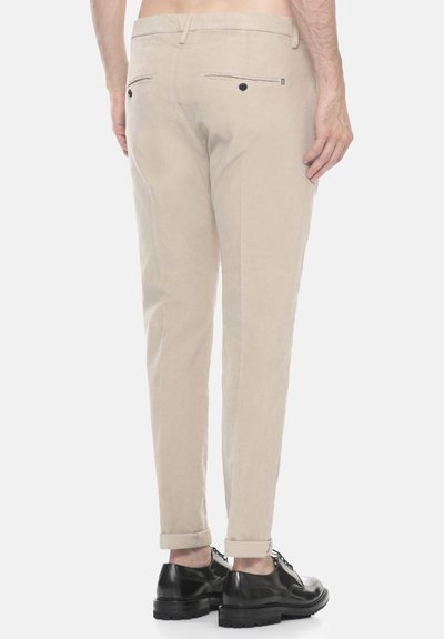 Pantaloni in lino beige con una vestibilità slim, dotati di due tasche posteriori con bottoni neri e polsini arrotolati. Abbinati a scarpe nere con lacci.