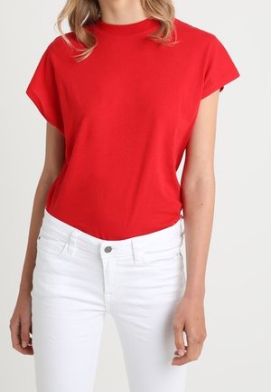 Red short-sleeve crewneck top paired with high-waisted white jeans on a person standing against a plain background.