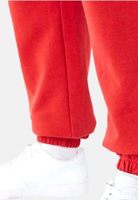Rode sweatpants met geribbelde boorden, gecombineerd met witte sneakers. Het materiaal lijkt zacht met een gladde textuur, ontworpen voor casual kleding.