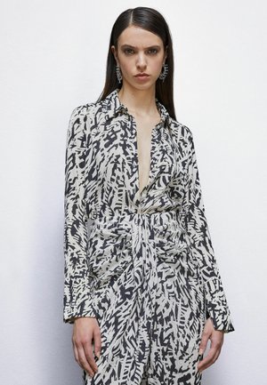 Camicia a maniche lunghe con colletto e scollatura a V profonda. Realizzata in tessuto stampato nero e crema. Presenta un dettaglio con vita arricciata e chiusura a bottoni.