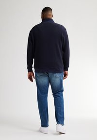 Marinblå texturerad tröja med krage, kombinerad med ljusblå jeans. Modellen ses bakifrån, vilket visar den avslappnade passformen och designen.