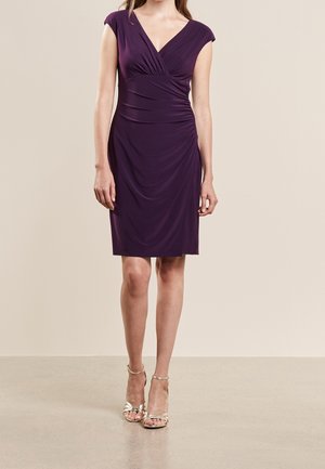 Fioletowa dopasowana sukienka z dekoltem w serek i krótkimi rękawkami. Cechą charakterystyczną są marszczone detale po bokach. Noszona z metalicznymi sandałami na obcasie z paskami.