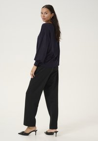 Navy oversized Pullover mit lockerer Passform, kombiniert mit schwarzen weiten Hosen und schwarzen High Heels, für einen lässigen Look gestylt.