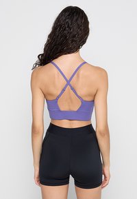Fioletowy biustonosz sportowy z wycięciem na plecach i skrzyżowanymi ramiączkami typu racerback. Do tego dopasowane czarne szorty.
