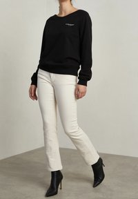 Schwarzes Sweatshirt mit langen Ärmeln und Rundhalsausschnitt, kombiniert mit eng anliegenden, cremefarbenen Jeans. Schwarze Stiefeletten mit spitzen Zehen.