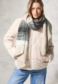 Rosa Cord-Jacke mit einem Rautensteppmuster, kombiniert mit einem weichen, gemusterten Schal in Grau- und Cremetönen. Blaue Jeans.
