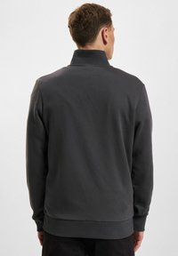 Felpa grigia con collo alto, maniche lunghe e polsini a coste. Texture liscia con un colore uniforme, senza motivi o accessori visibili.