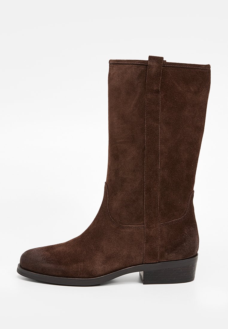 Stivale marrone in pelle scamosciata alto fino al ginocchio, con punta rotonda, tacco piatto e cuciture rinforzate. Texture liscia con un leggero lucido e accenti minimi.