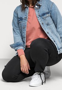 Chaqueta de mezclilla en azul claro con botones de metal, llevada sobre un sudadera rosa. Joggers negros ajustados y zapatillas blancas con detalles negros.