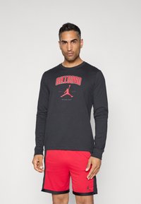 Schwarzes Langarm-T-Shirt mit rotem "CHICAGO"-Druck und Jordan-Logo, kombiniert mit roten Mesh-Shorts. Beide Teile haben ein sportliches Design.