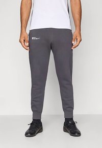 Sivé tepláky z bavlnenej zmesi, s zužujúcim sa strihom a rebrovanými manžetami. Logo Nike a nápis "INTER" sú potlačené bielou farbou. Čierne topánky.