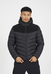 Camisa acolchada negra con un yugo de forro polar negro texturizado, cierre de cremallera, capucha elástica y puños acanalados. Presenta un corte ajustado y acolchado horizontal.