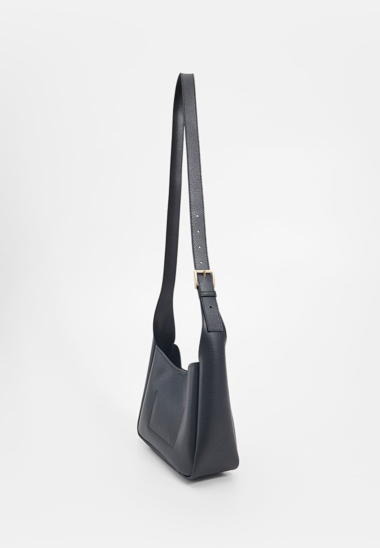 Schwarze Lederhandtasche mit strukturierter Oberfläche, trapezförmiger Form, langem Schulterriemen und einer kleinen Fronttasche. Sichtbare verstellbare Riemenhardware.