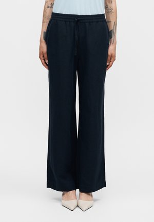 Čierne široké nohavice s elastickým pásom a šnúrkou, nosené s bielymi špicatými topánkami a svetlomodrým topom.