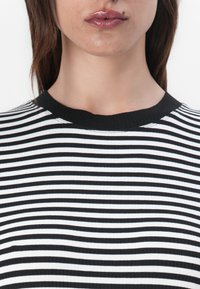Svart-hvitt stripet ribbet topp med rund hals og strukturert stoff. Stripene er jevnt fordelt og horisontale.