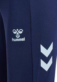 Marineblauer Stoff mit weißem hummel-Logo und zwei weißen Chevron-Streifen auf Sportbekleidungs-Material.