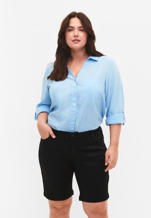 Light blue long-sleeve shirt with button closures and chest pocket, paired with black knee-length shorts, front view against a white background.