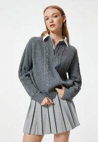 Grå stickad tröja med kabelmönster, en v-ringning och långa ärmar, kombinerad med en veckad grå kjol.