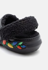 Črn puhast natikač z teksturirano naramnico. Na strani vsebuje pisane dizajne žarnic. Mehka, topla obleka. Okrogla oblika.