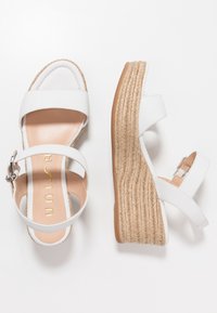 Valkoiset viistokärkiset sandaalit, joissa on kaksi leveää remmiä, teksturoitu espadrille-alusta ja metallinen solki sivussa. Sujuva nahkapinta.