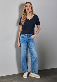Námořnické tričko s výstřihem do V spárované se světle modrými širokými džíny a bílými teniskami. Měkká bavlněná tkanina s volným střihem a minimálním zdobením.