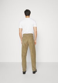 Pantaloni in corduroy marrone con vestibilità dritta, dotati di cintura e tasche posteriori, abbinati a una t-shirt bianca semplice e scarpe nere.