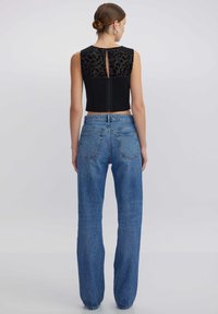 Top corto negro con un panel de estampado de leopardo y cremallera en la espalda, combinado con unos jeans azules de tiro alto que presentan un diseño clásico de cinco bolsillos.