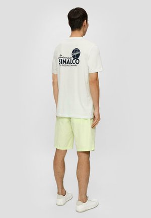 Off-white trumpas rankovėmis marškinėliai su tamsiai mėlynu Sinalco logotipu ant nugaros. Derinami su šviesiai geltonomis šortais ir baltais sportbačiais.
