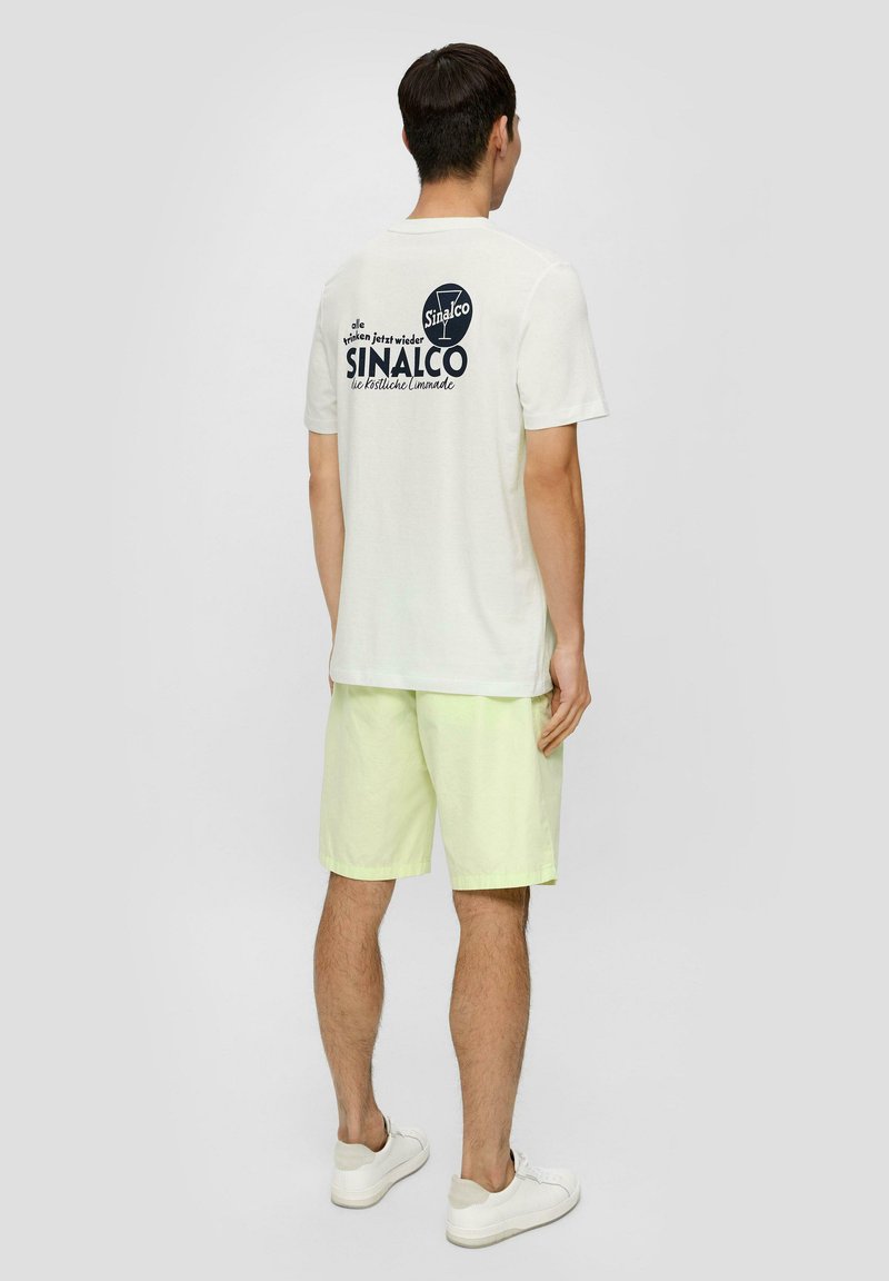 Off-white trumpas rankovėmis marškinėliai su tamsiai mėlynu Sinalco logotipu ant nugaros. Derinami su šviesiai geltonomis šortais ir baltais sportbačiais.