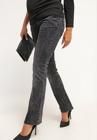 Jeans neri elasticizzati con effetto scolorito, design a gamba dritta e discreti dettagli di cucitura, abbinati a scarpe con tacco alto e una clutch nera.