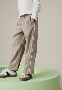 Pantalons beiges amples avec une taille élastique et des boutons décoratifs sur le côté, associés à des baskets blanches avec une rayure noire.