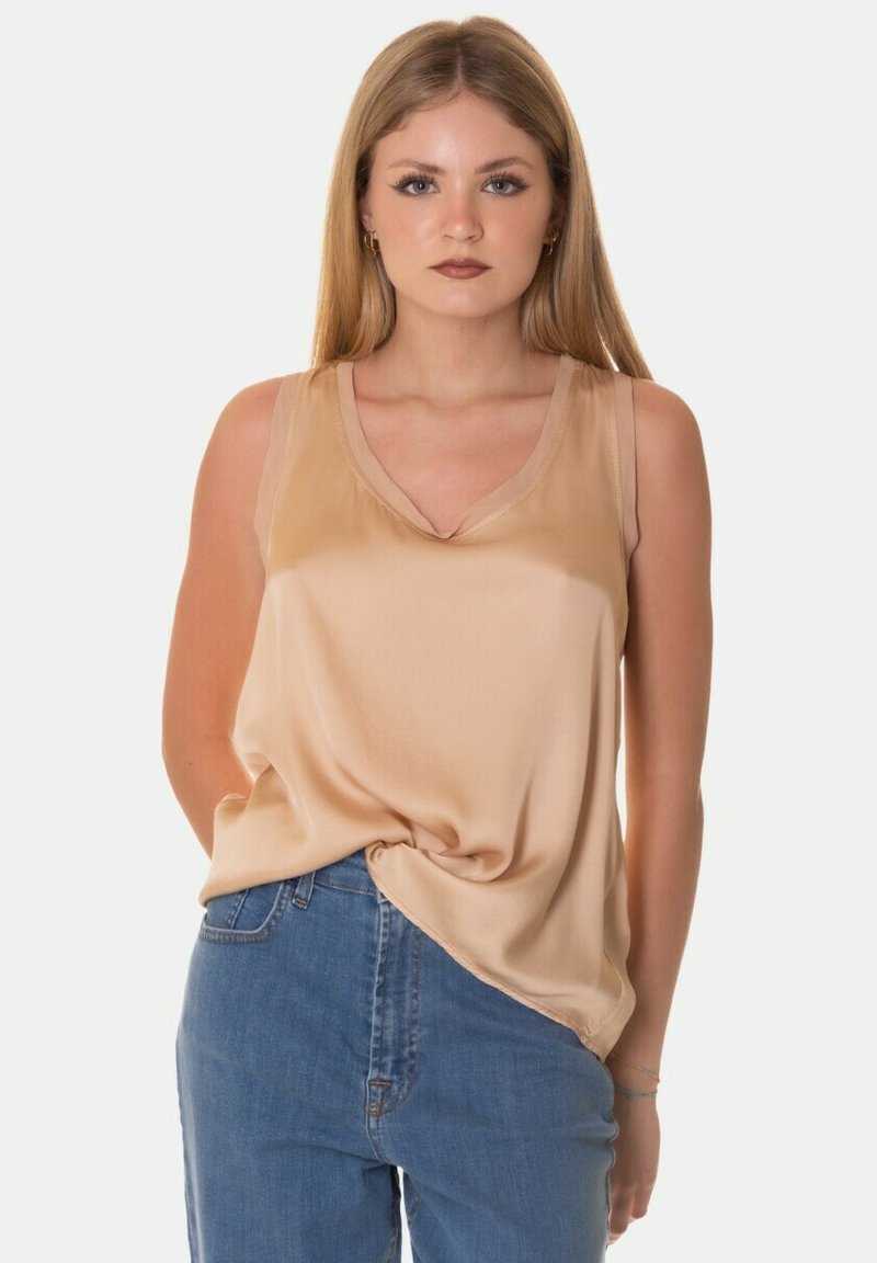 Top in satin beige senza maniche con scollatura a V, caratterizzato da una vestibilità rilassata e una texture morbida; abbinato a jeans blu a vita alta.