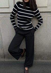 Zwart-wit gestreepte geribbelde coltrui gecombineerd met zwarte wijde broek en zwarte instap schoenen. Soepele texturen en op maat gemaakte pasvorm.